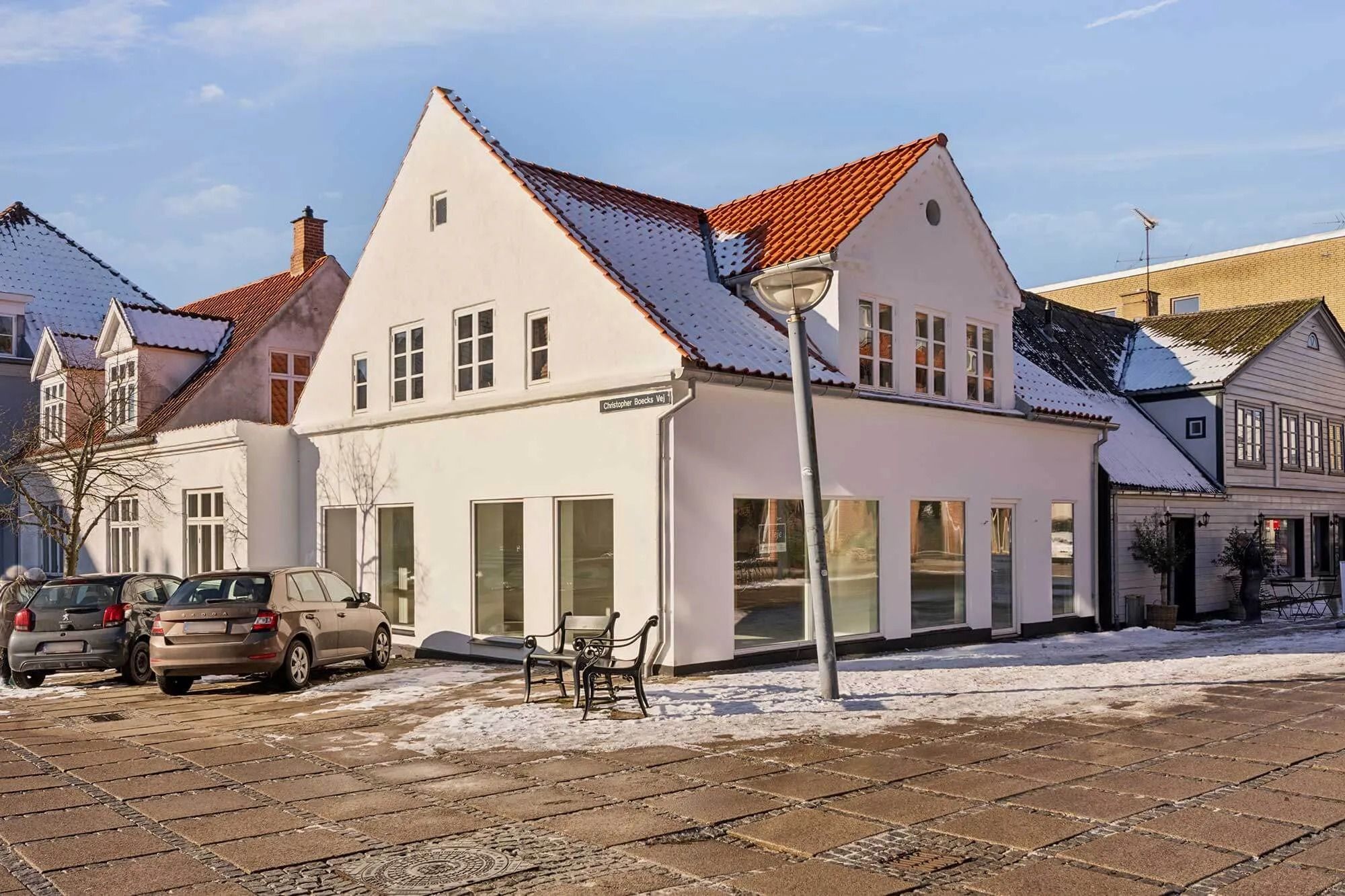I Fredensborg ligger et butikslokale med store ruder og to parkerede biler på vejen foran