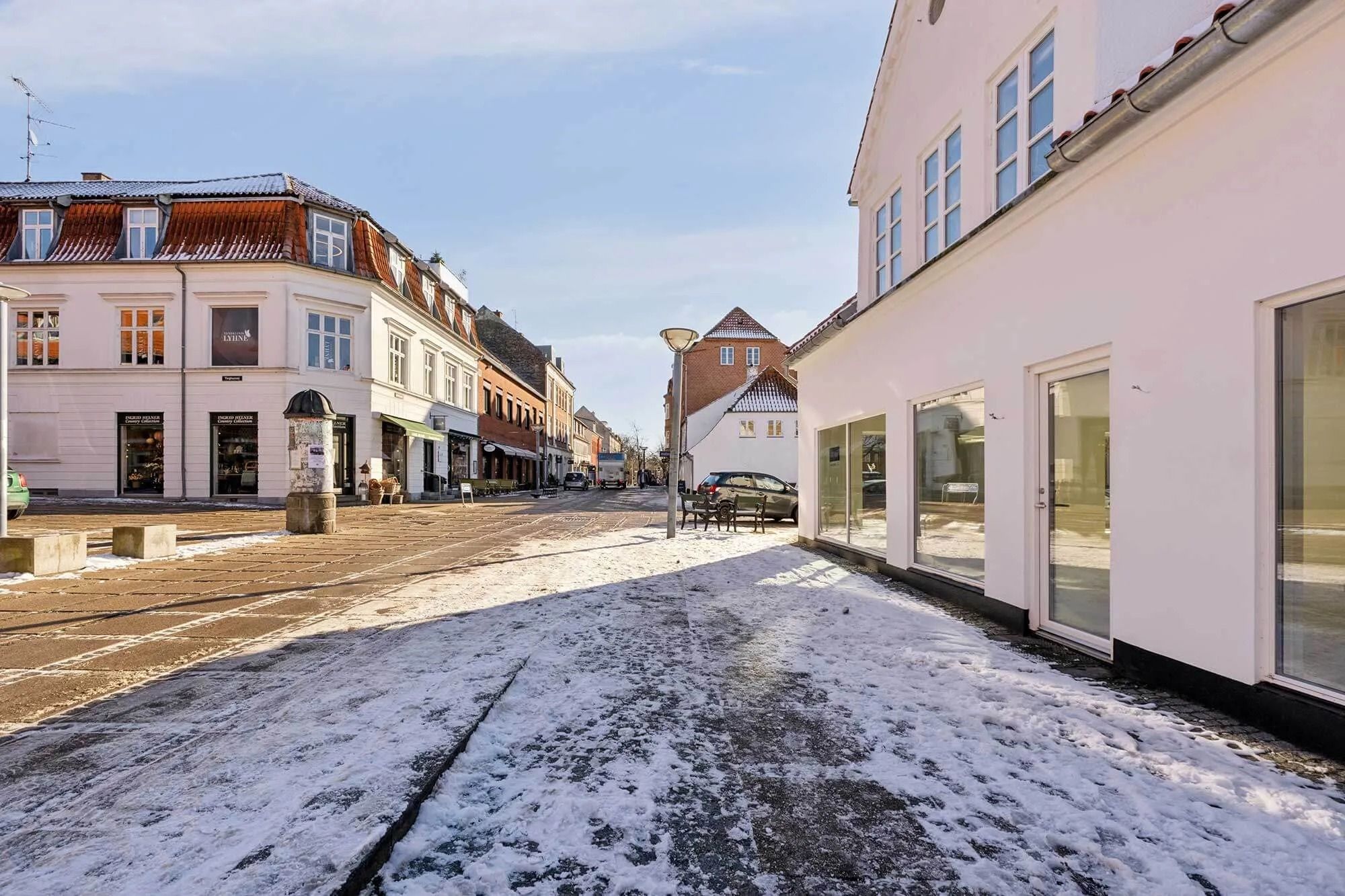 En snelagt gade med smukke huse og butikker, der er dækket af sne og refleksioner fra vinduer og lygter