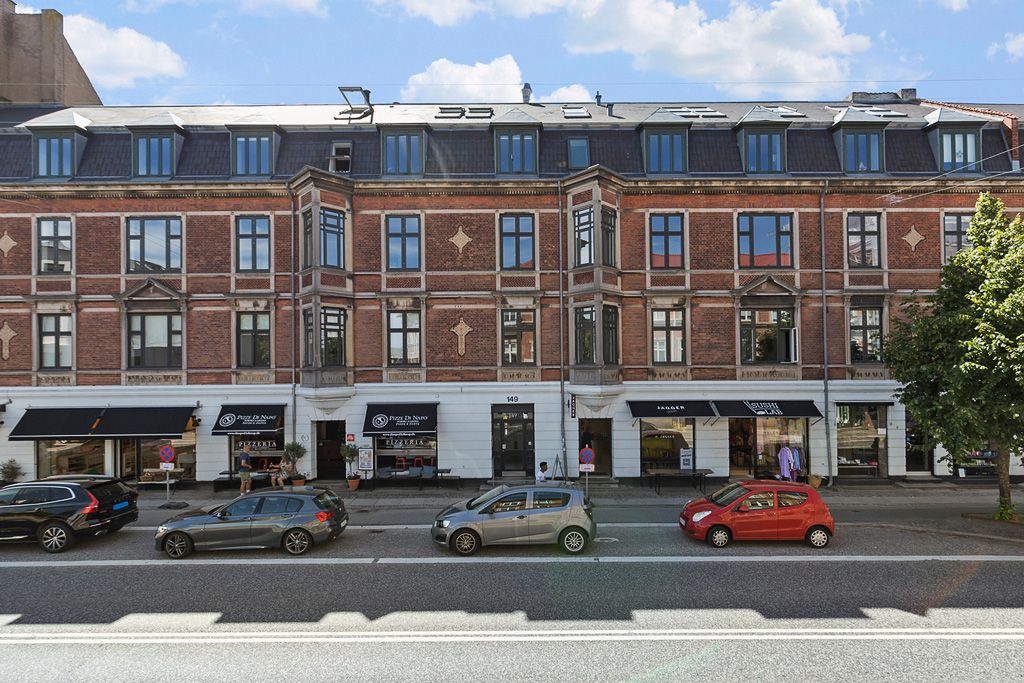 Menighedsbygning med røde mursten og flere butikker på 1. sal. Fire biler er parkeret foran bygningen