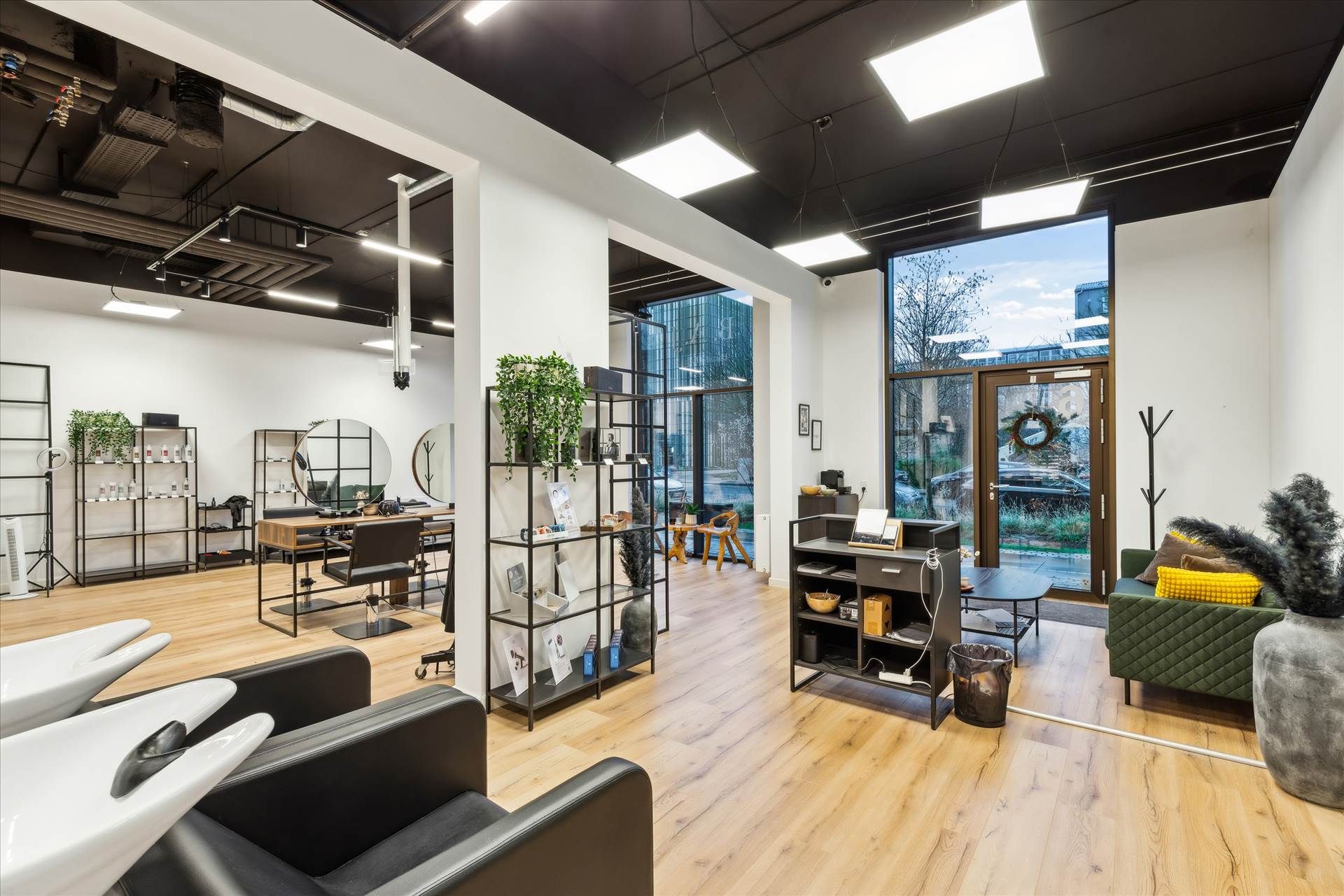 Salon med moderne møbler og en stor spejl og plante. To stolpelyse og lyse loftslampe. En køkkendel med en sofa og en