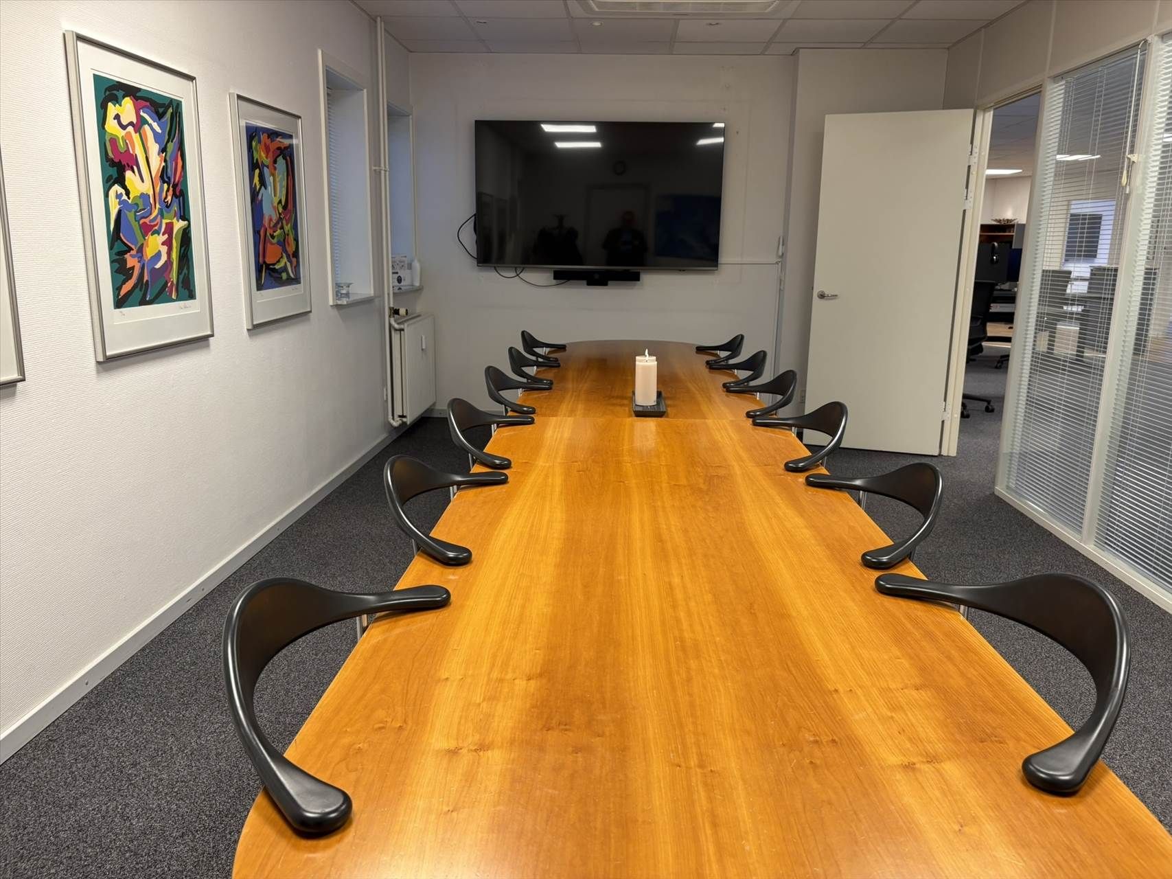 Kontor med længdebord og stole. Bord med lysekanter og lysegult vægmaleri. Et af billederne er abstrakt.