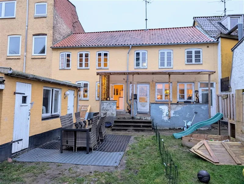 Foto af en have med græs, grønne planter og en grøn rutschebane samt en havemøbelsæt med en bord og stole