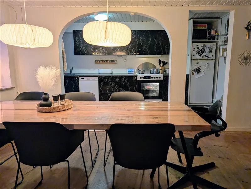 Moderne køkken med lyse loftslamper, en hvid køleskab og en sort ovn med en gryde på hylden ovenpå