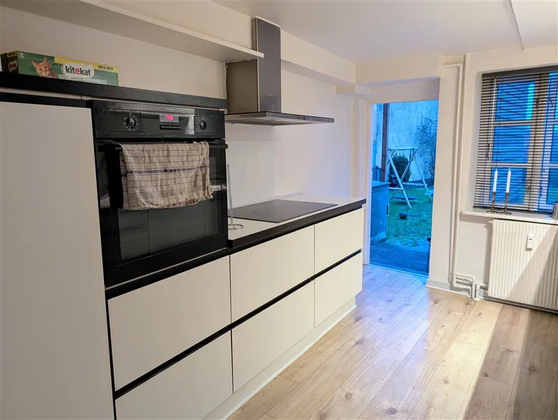 Et moderne køkken med en sort ovn, en spisestue med trægulv, en stang og et vindue med solskærme