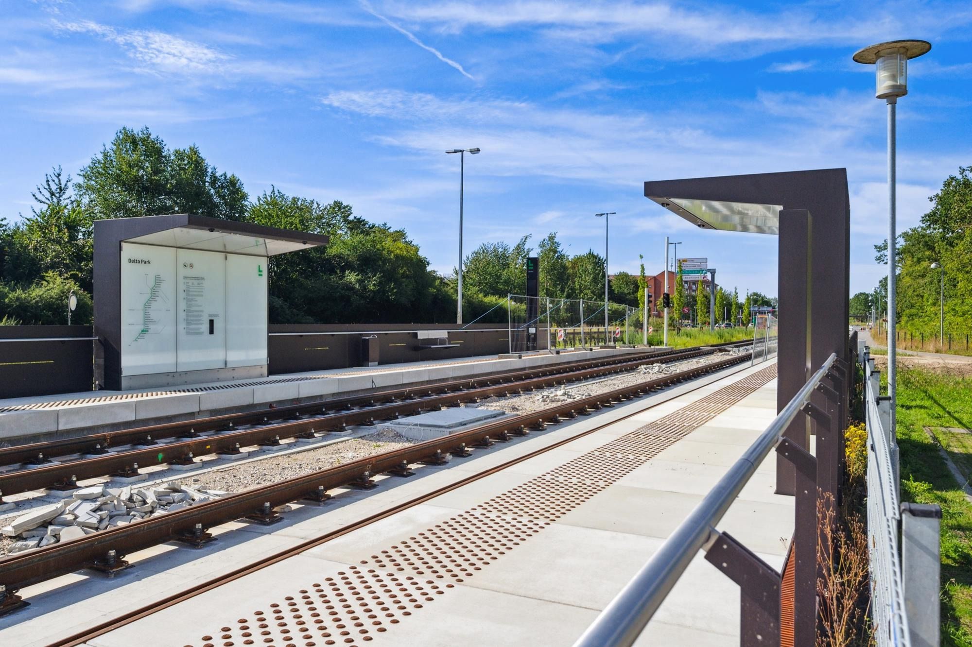 Togstation med spor, bænke, lygter og reb, der adskiller perronen fra sporene. Der er også et infoskilt, der viser Delta