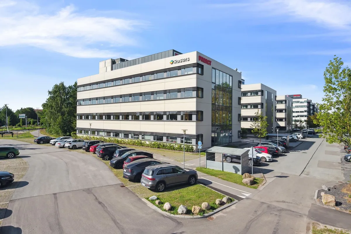 Kontorbygning med facader i lysebrune og hvide farver og logoet Resulis. Foran bygningen er der parkeringspladser og grønne