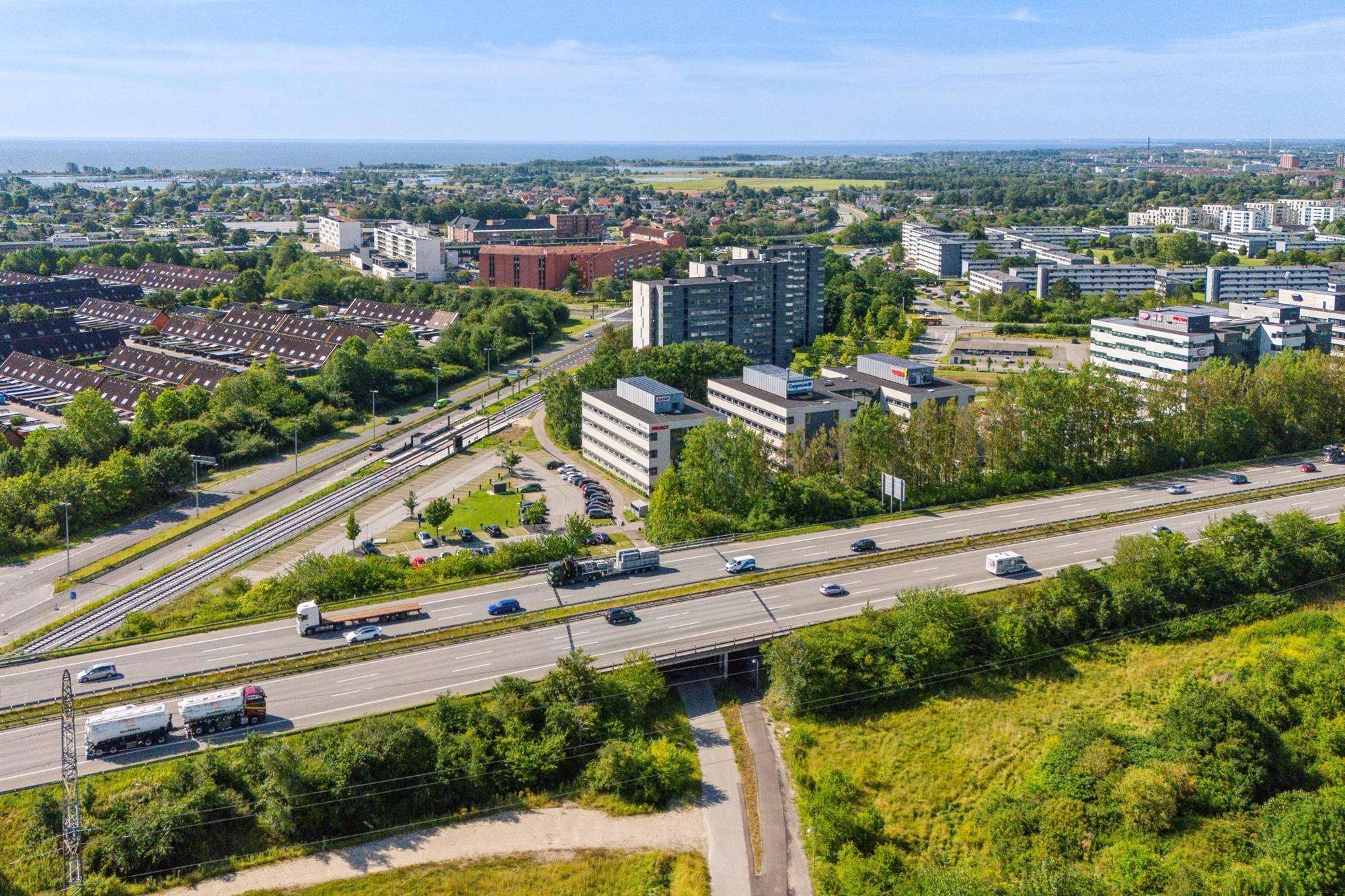 Delvist set by fra luften med bygninger, veje, biler og busser og et hav i horisonten