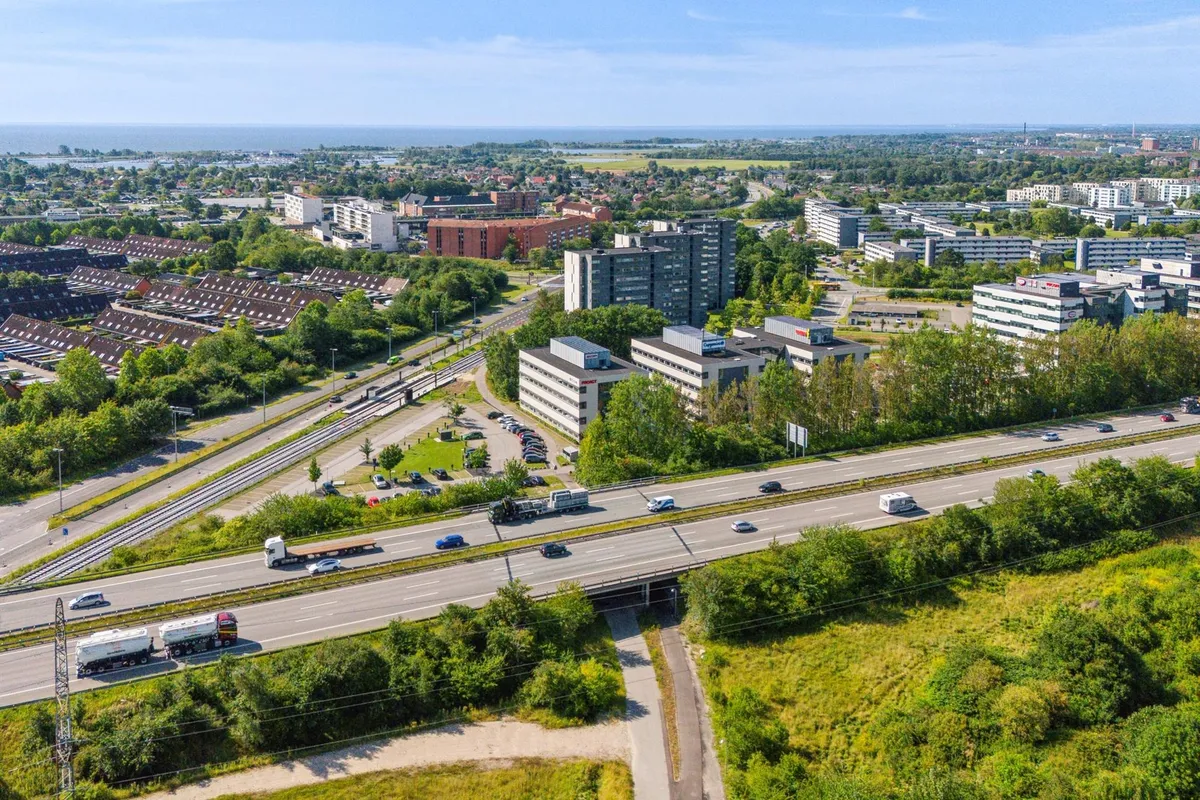 Delvist set by fra luften med bygninger, veje, biler og busser og et hav i horisonten