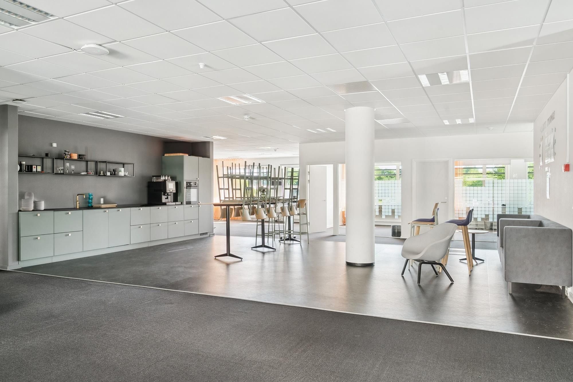 Kontorlokaler med moderne møbler, højloftede rum, hvide lofter, grønne vægge, et køkken med apparater og en sofa til hvile.