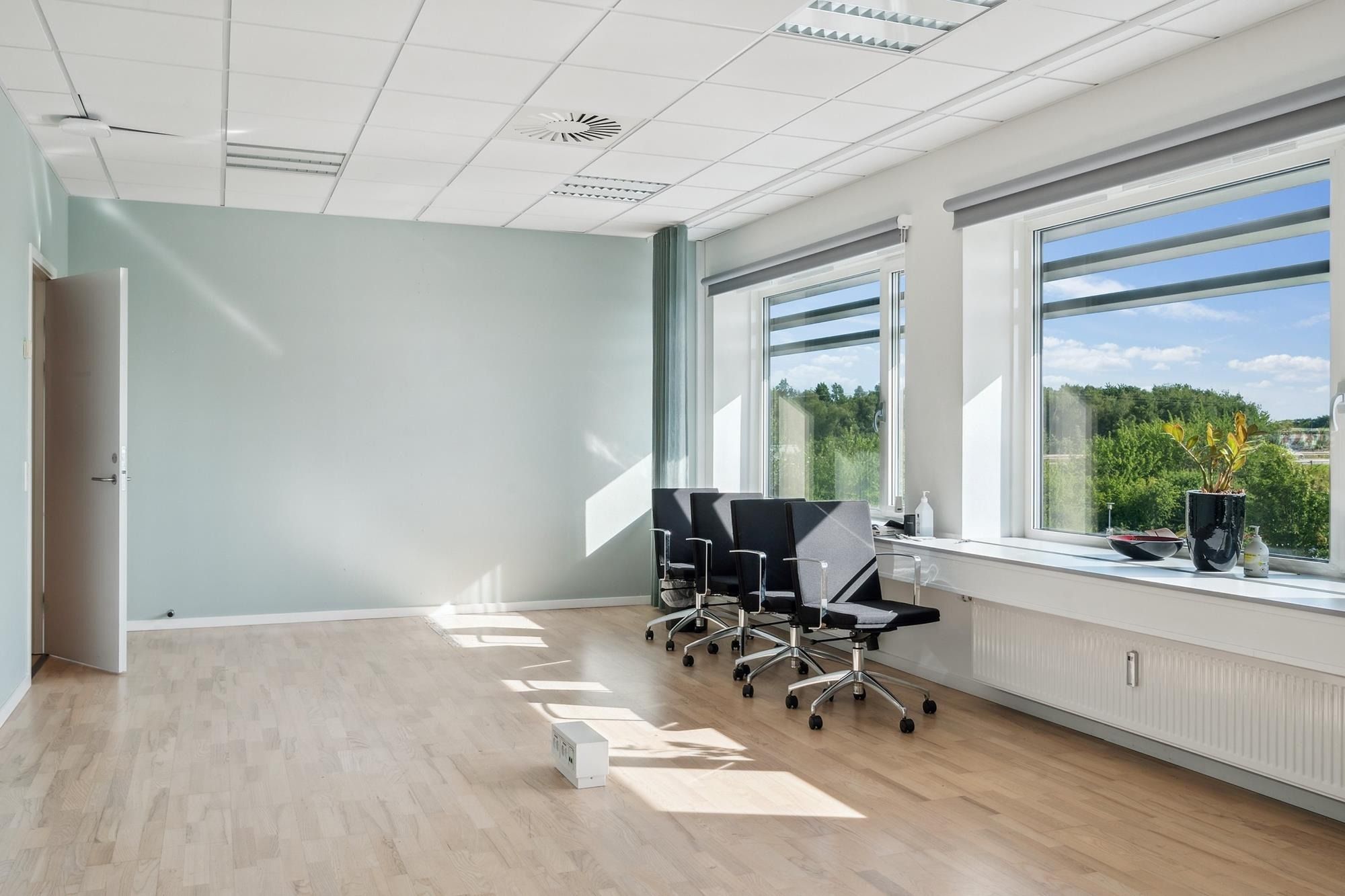 En kontorvirksomhed med højt til loftet og store vinduer. Kontoret er fuldstændig tomt med fire ergonomiske kontorstole. Der