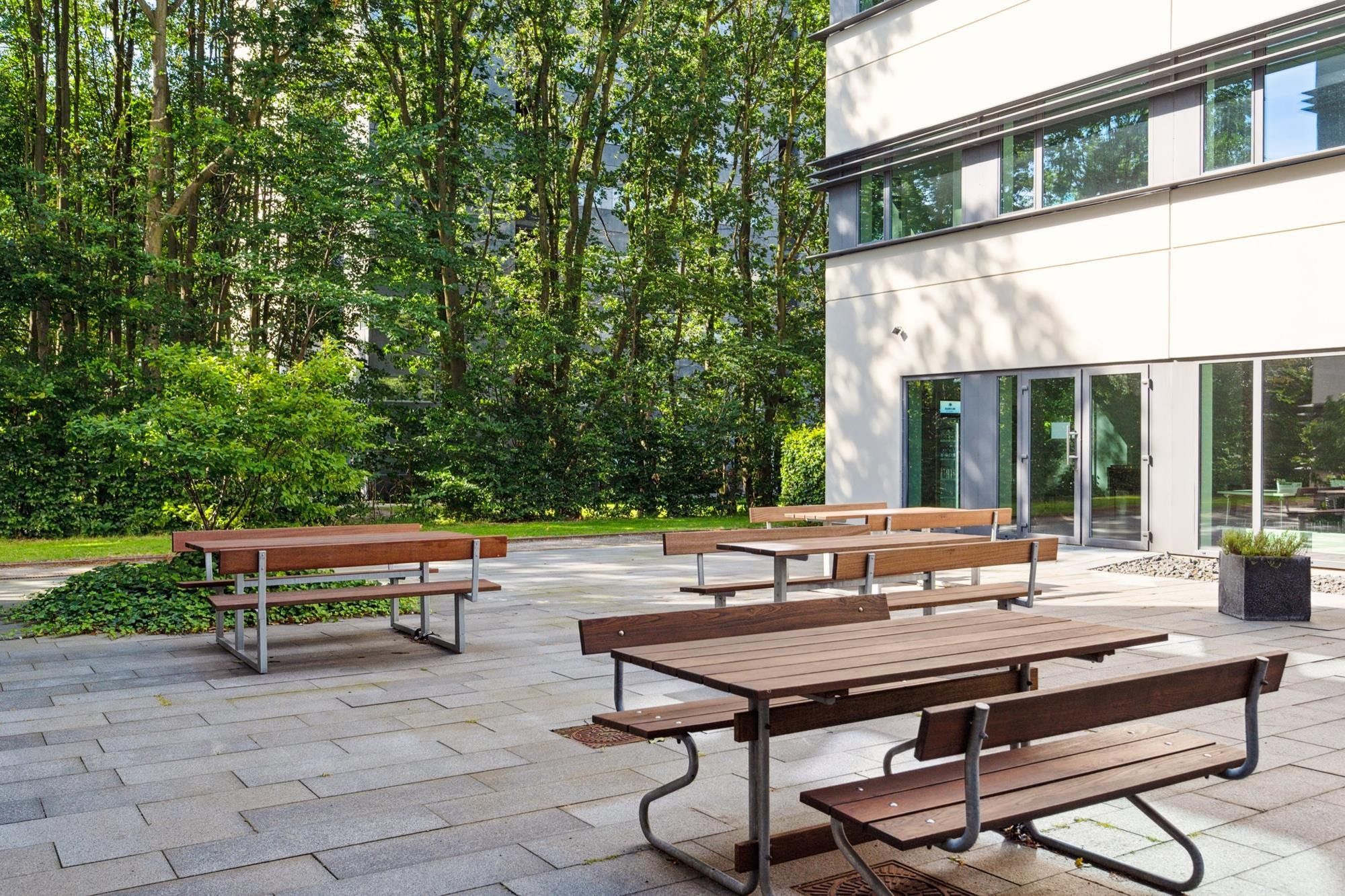 Plads med bord og bænke til møder og pauser udendørs ved et moderne bygningskompleks med mange vinduer