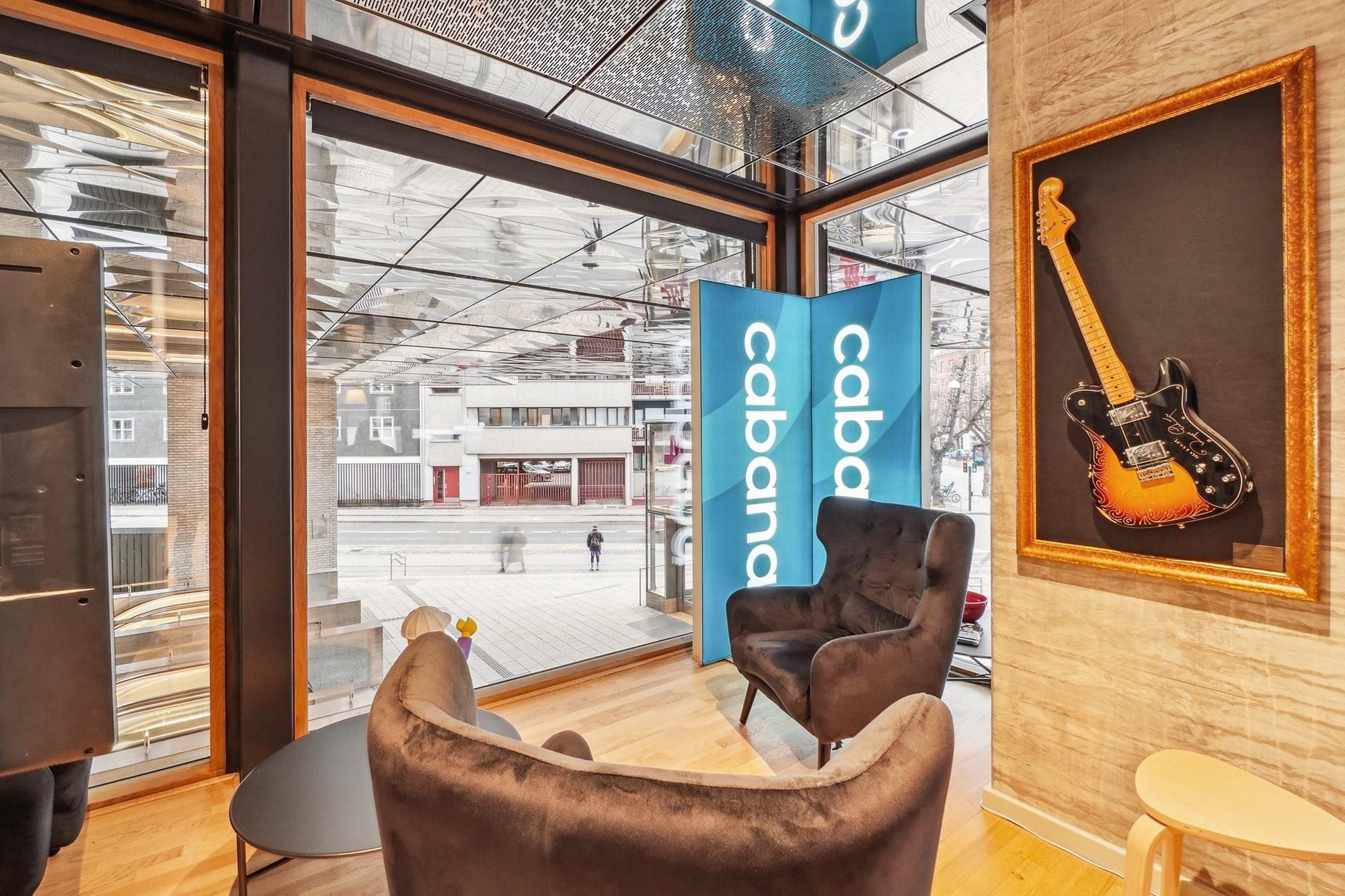 En stue med to brune lænestolpe og en guldframmede kunstvæg med en elektrisk guitar og en blå banner med teksten "cabana"