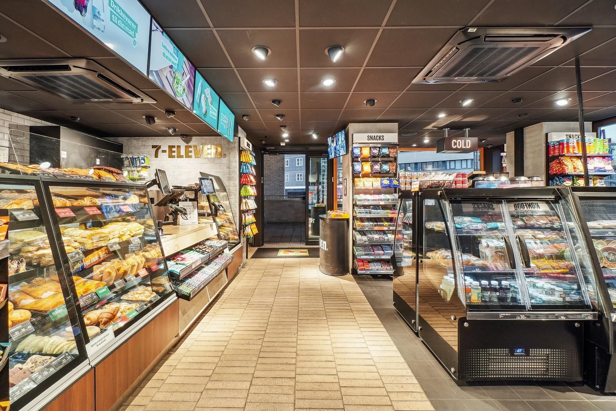 Indvendørs 7-eleven butik med krydsfiner og træindfattede salgsskuffer med mad og drikkevarer. Butikken har klimaanlæg i