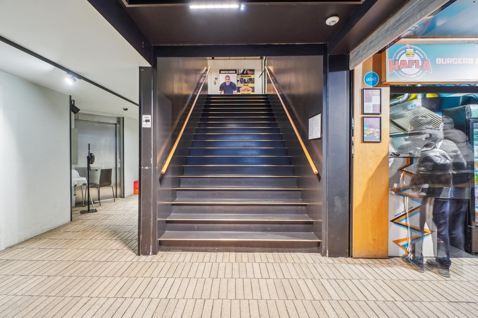Indgang til en restaurant med trapper og vinduer, hvor en mand står og smilte i døren, og en skrift, der læser "Hafla
