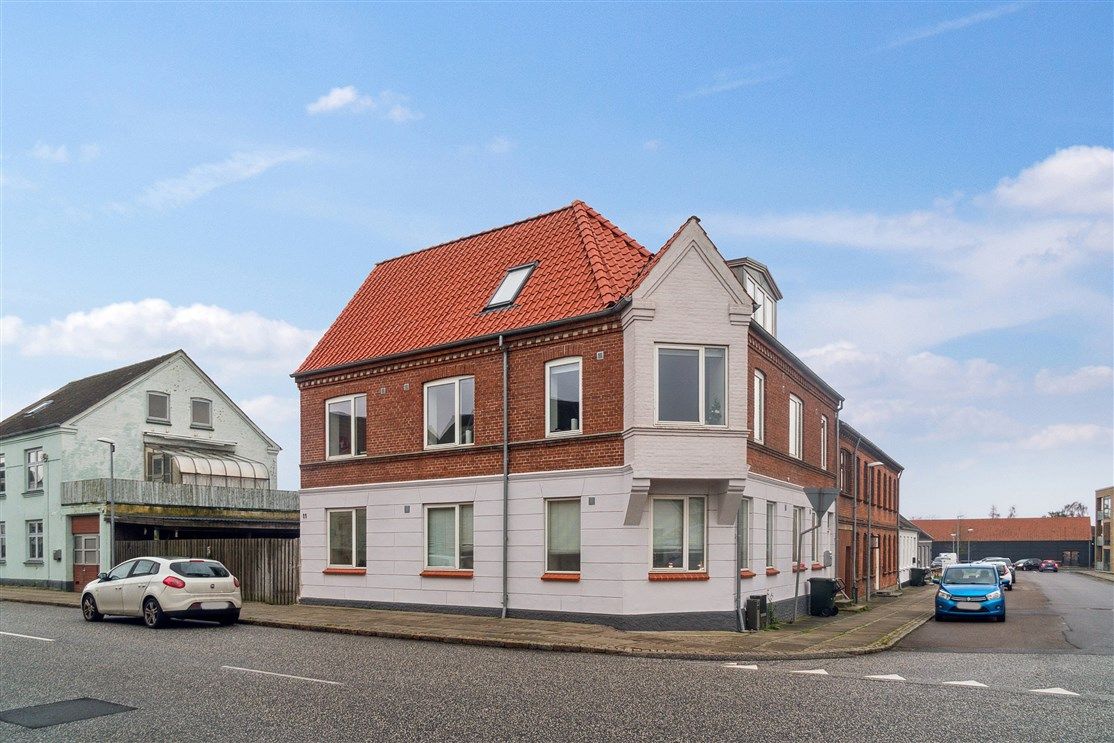 Et rødt tag, en hvid og rød facade, flere parkerede biler og et rødt tegltag