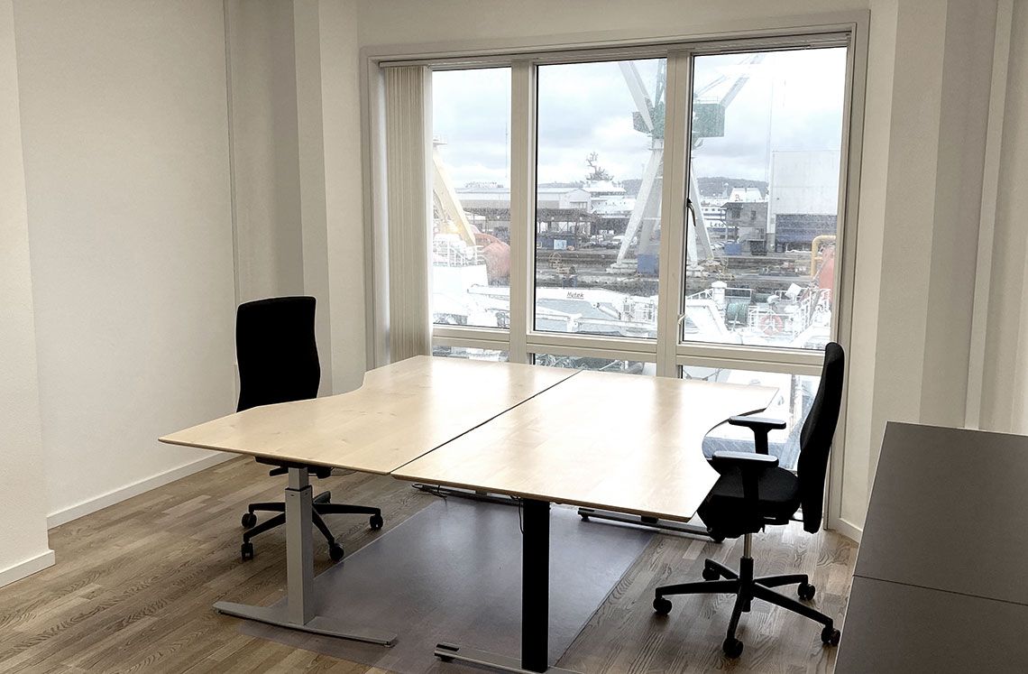 Moderne kontor med to bord og stole samt stort vindue med udsigt til skibe og bygninger.