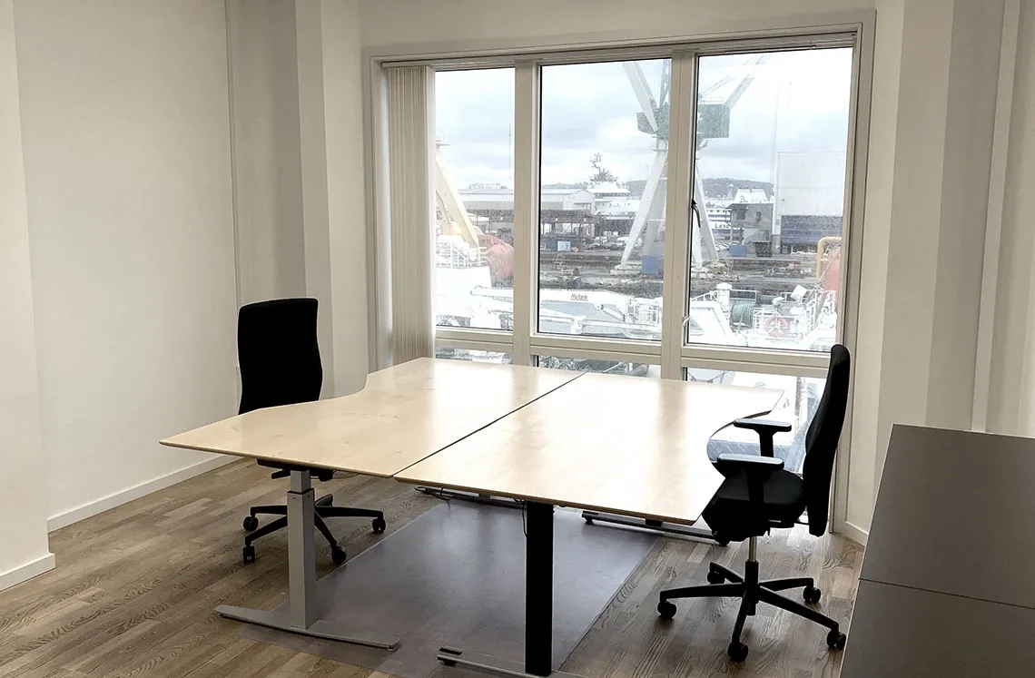 Moderne kontor med to bord og stole samt stort vindue med udsigt til skibe og bygninger.