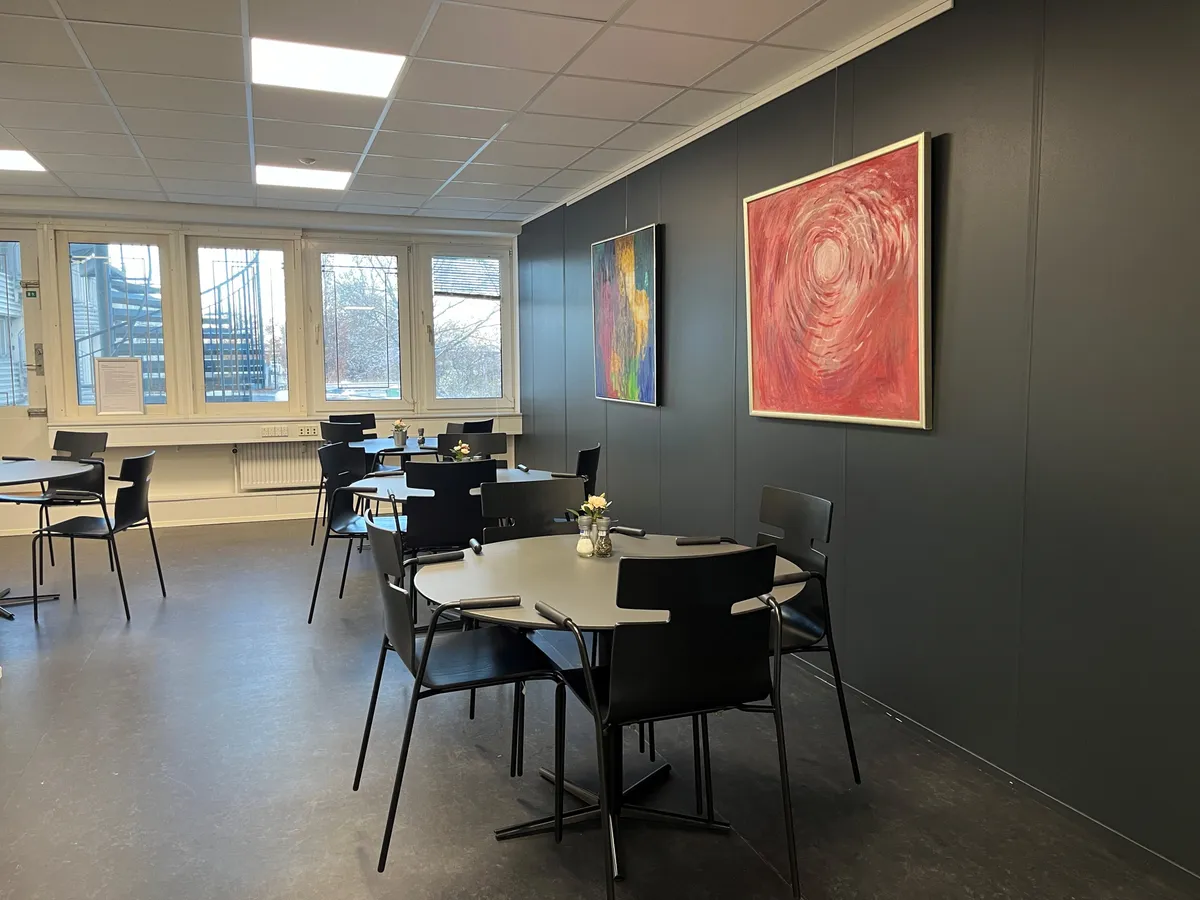 Det lyse lokale med runde borde og lyse gulve samt to lyse malerier på væggen