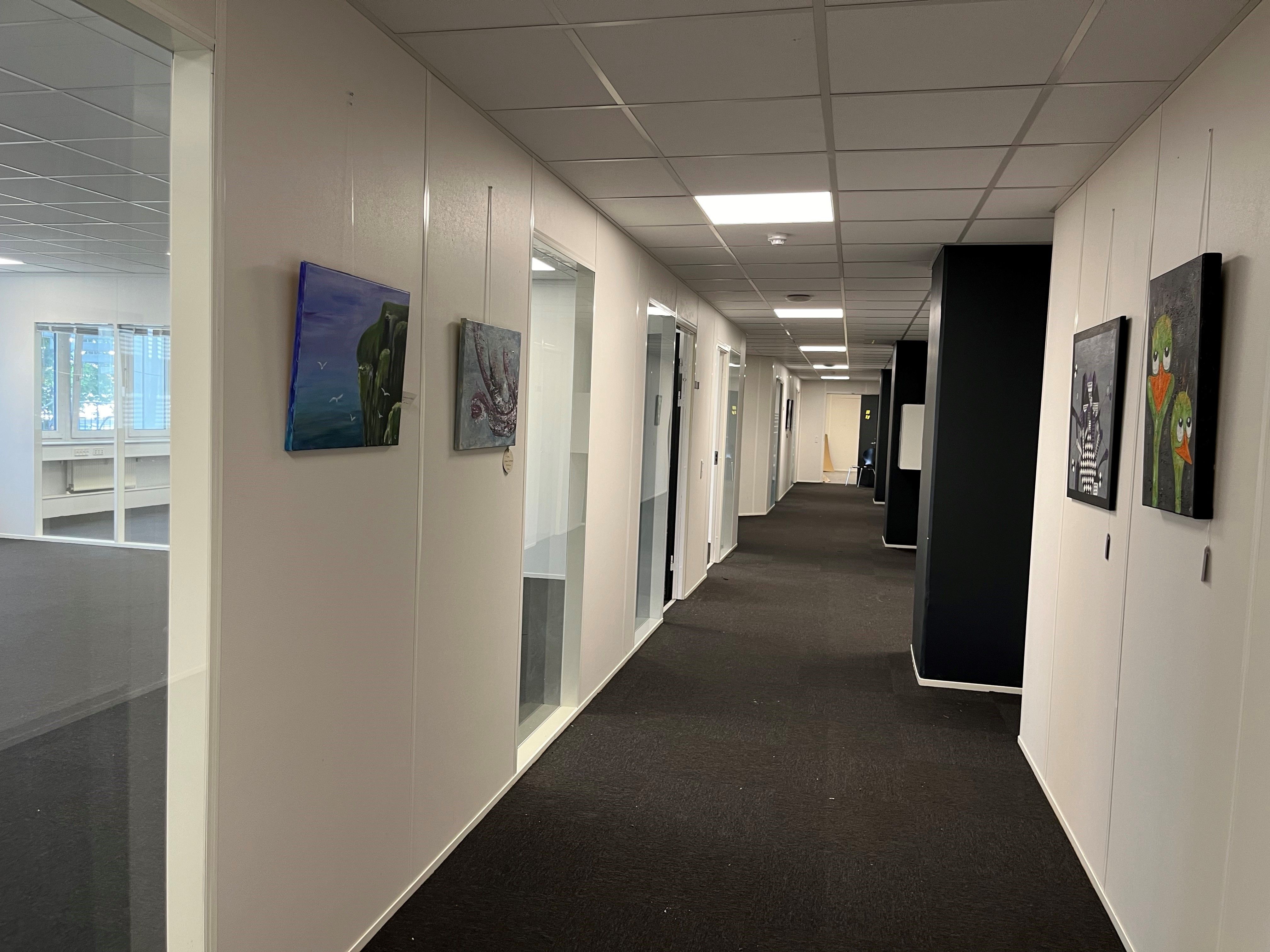 Hvidt og svart indretning med lysegult lys i en stille korridor med kunstværker og møbler i enden