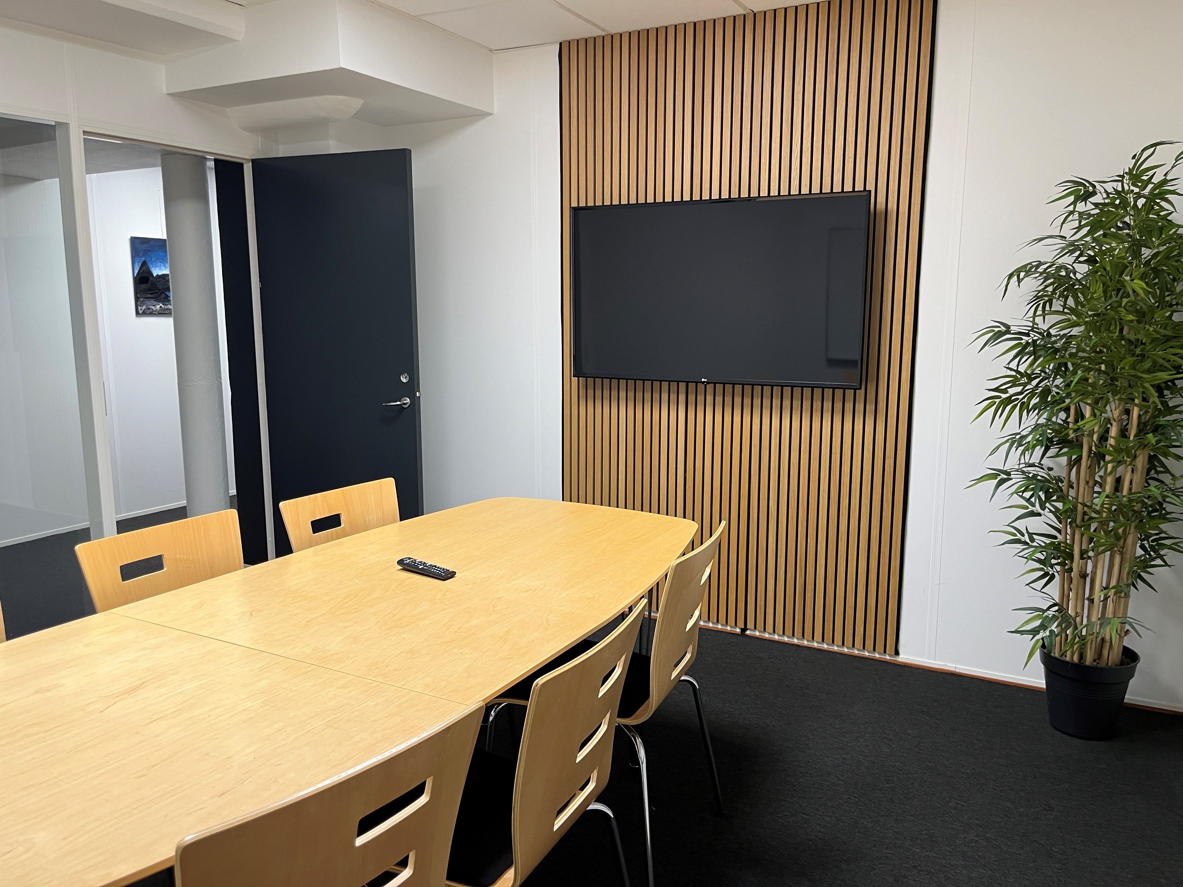 Modernisering af konferencelokale med trævæg og fjernsynsapparat samt stolpe med plante