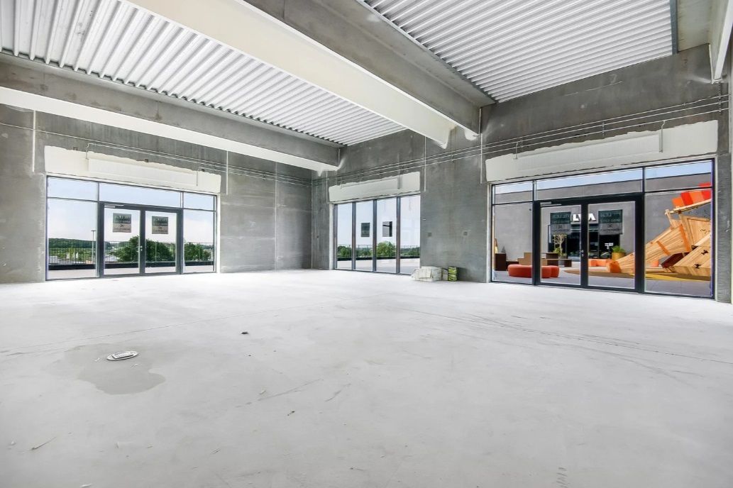 En stor, nybygget detailhandelslokale med højloft og store vinduer, der reflekterer lys og viser udsigt til bygninger og