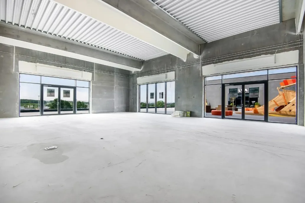 En stor, nybygget detailhandelslokale med højloft og store vinduer, der reflekterer lys og viser udsigt til bygninger og