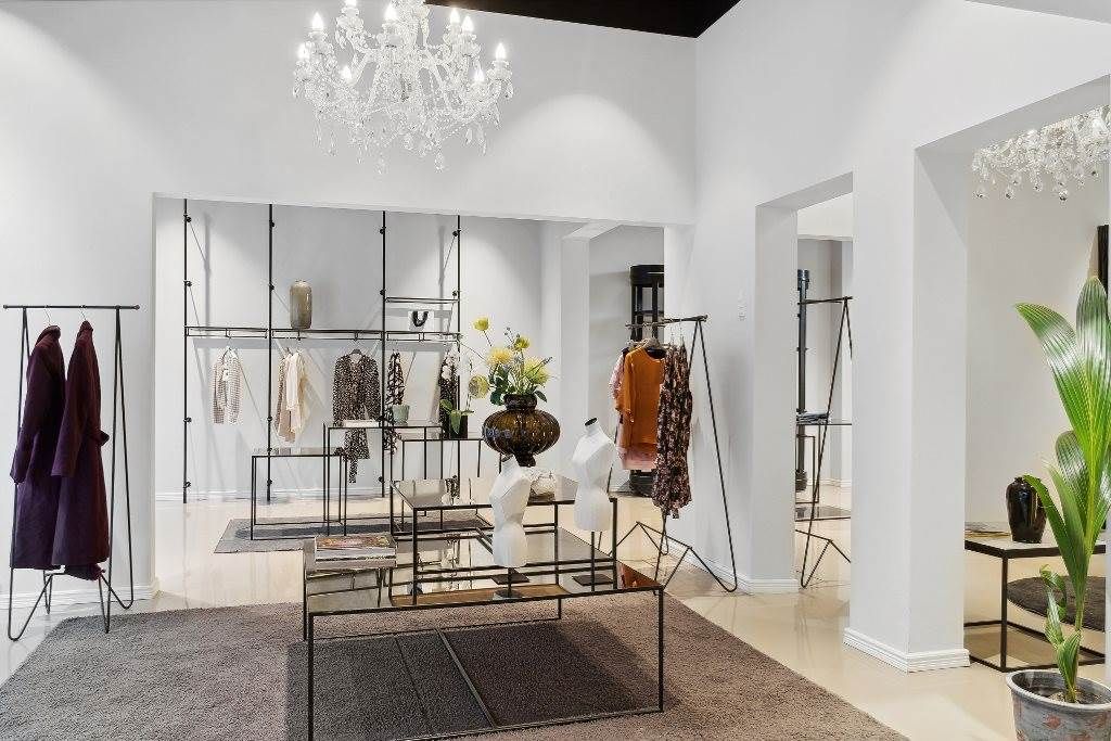 Et veludstyret interiør med store lysekroner, tæpper og stilfulde møbler, hvor tøj er udsat på hylder og stativer