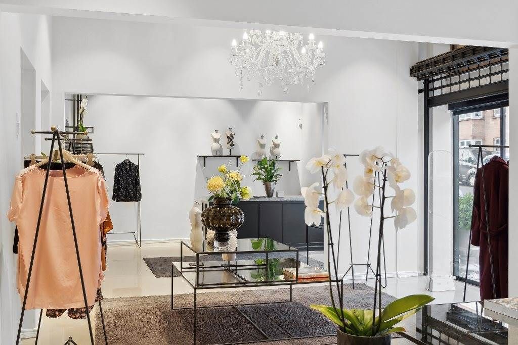 Elegant butik med tøj på hængere, lyse blomster og krystalkrone i loftet, smukke møbler og udsmykninger.
