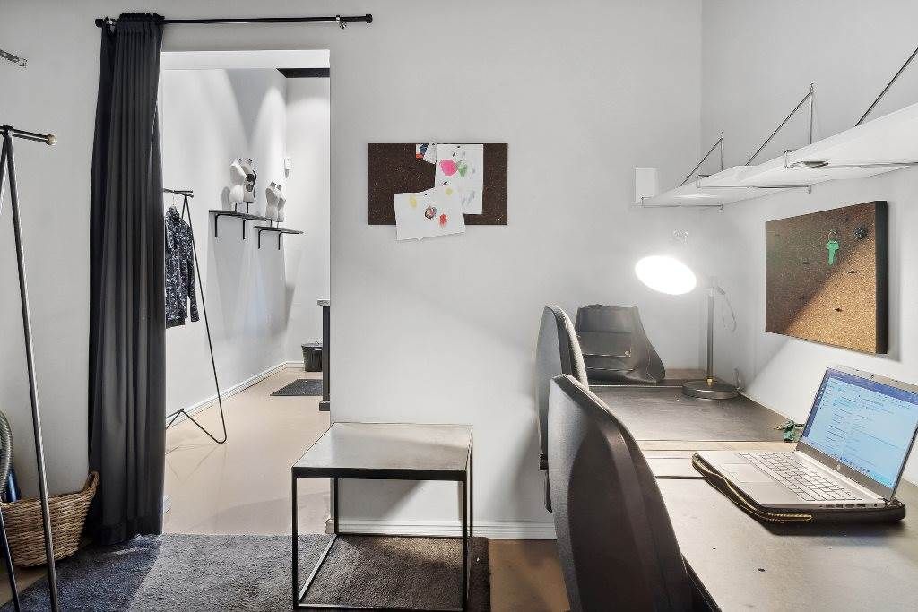 To kontorsteder med skriveborde, lysestager og stole, samt en åben dør og tøjreol.