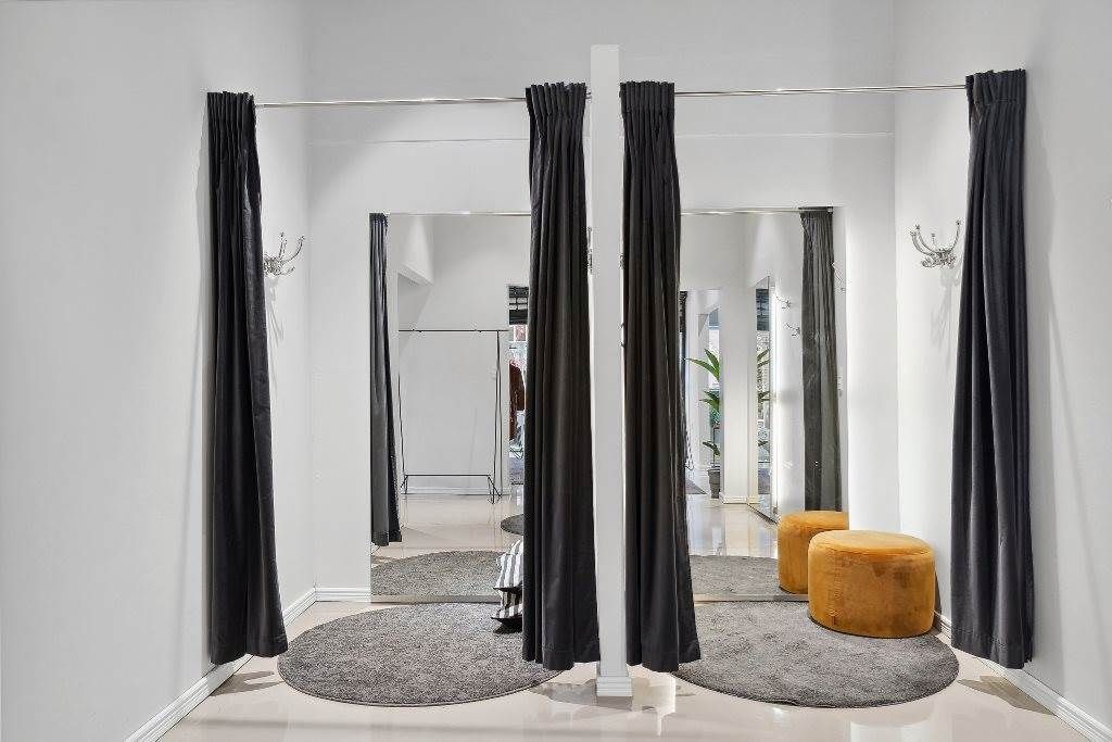 En moderne, minimalistisk stue med hvide vægge og gulv, to store spejle og to store sorte gardiner i midten, samt to runde,