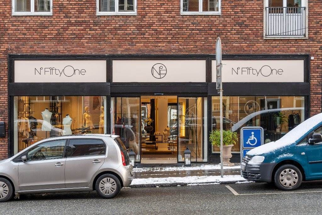 To biler parkeret på en gågade med N Fifty One butik, en med handicapsymbol og sne på fortauet