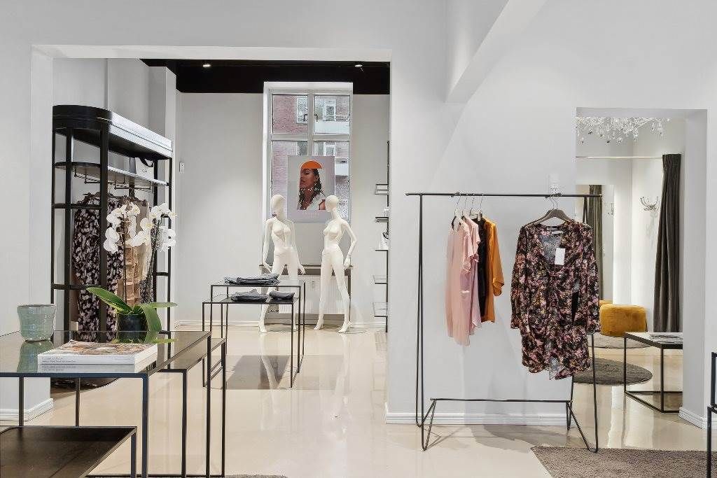 Et moderne og velinreddet tøjforretningslokal med hvidt loft og vægge, og håndsyede kjoler og bukser på en simpel og enkel