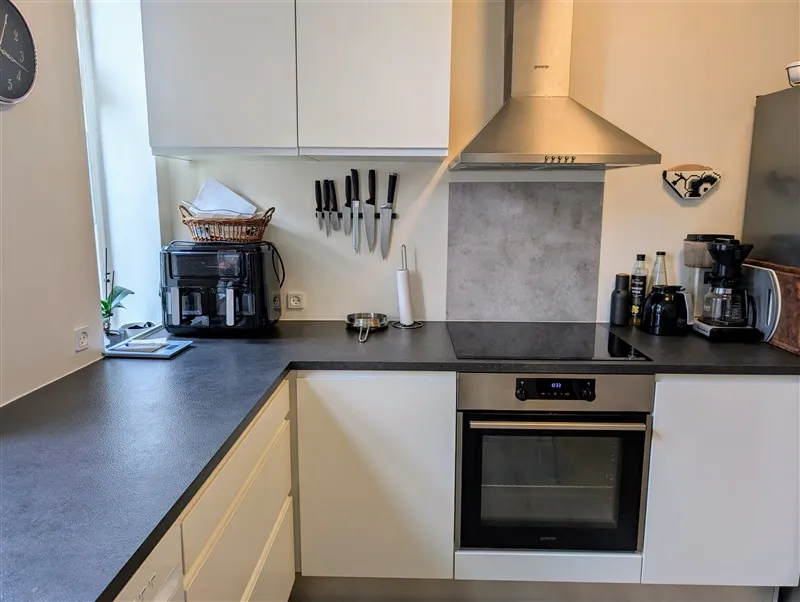 Moderne køkken med sort skab, høj skorsten, gaskomfur, mikrobølgeovn, kaffemaskine, køleskab og ur på væggen