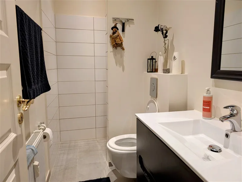 Renoveret badeværelse med hvidt badekar og håndvask, sort højre og sort spejl med et væghylde med lysekroner og vase