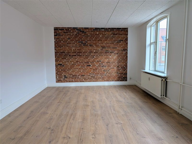 Store lyse stue med moderne gulvbelægning og lyse vægge, røde mursten og hvid gulv samt store vinduer