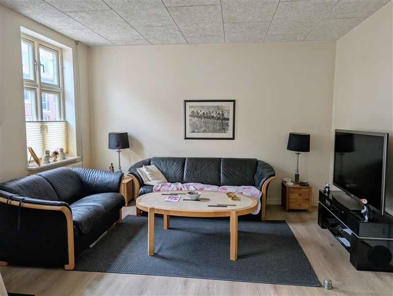 På dette foto ser du et lyse stue med to sort lædersofaer, en træbord, en tv og to lamper.