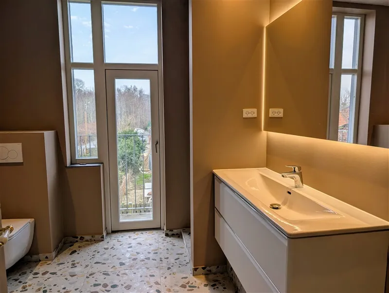 Badrum med toilet, vask, spejl og lyspærer. Et lyse, moderne badrum med lysegul væg, lysgrå gulv og hvidt toilet.