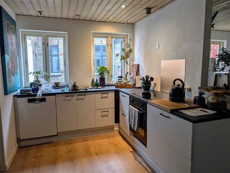 Køkken med hvide skabe og sort stolpe, møbler og udstyr, lysevinduer og lysegulve