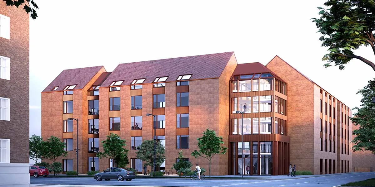 Moderne bygning med tre fløje, store vinduer, parkeringsplads, cykelstier og fortove, folk går og cykler langs gaden, biler