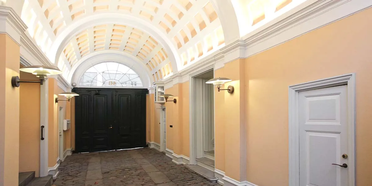 En lysegul hall med krydshvælving og hvide vægge, to dobbeltdøre og en lysekron samt to væglamper, der giver god belysning
