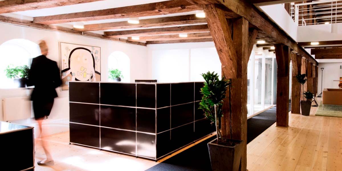 Et moderne kontor med lyse loftsbjælke, gult vægmaleri, sort marmor og glas modtagebord, stående potteplanter og trægulv