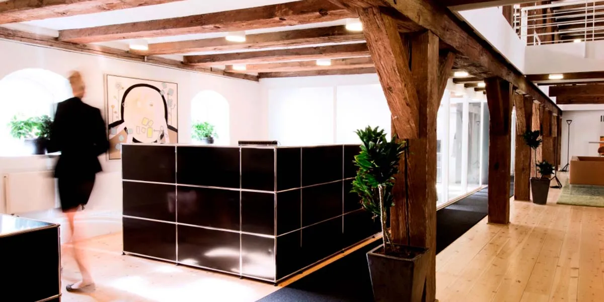 Et moderne kontor med lyse loftsbjælke, gult vægmaleri, sort marmor og glas modtagebord, stående potteplanter og trægulv