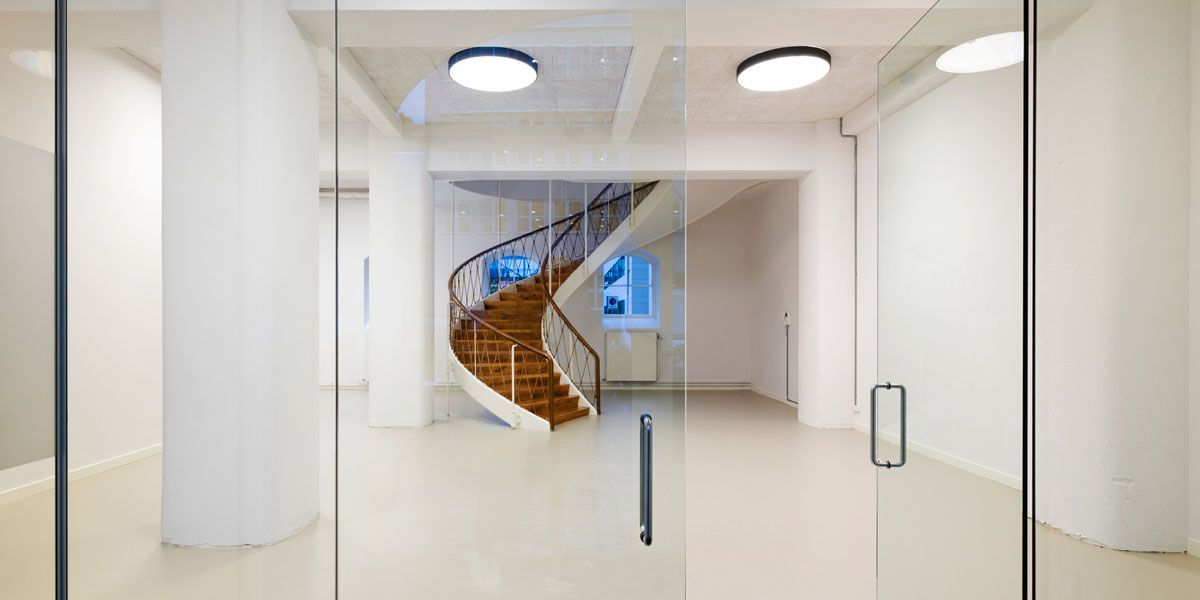 Det er et interiør med spiraltrappe og hvide vægge og gulv samt to høje lysekroner