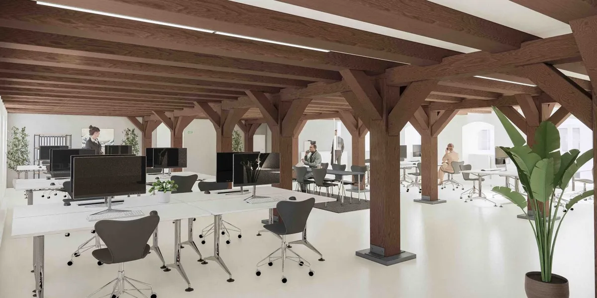 Store træbjælker, højt loft, hvide vægge og gulv, moderne kontormøbler og computere, plante i gryde, flere mennesker i en