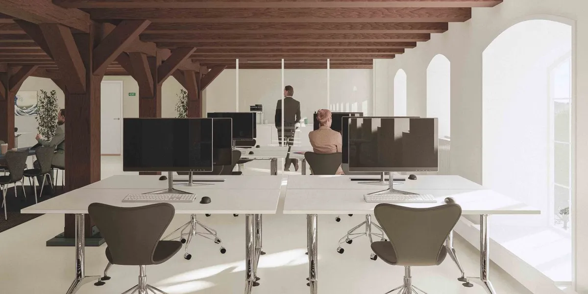 Et moderne kontor med højt til loftet og lyse gulve, to skriveborde med computere og en person i bukser og en skjorte