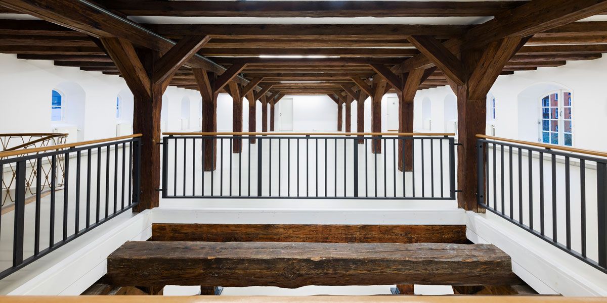 Indvendigt af et bygningsværk med bjælkeloft og bjælkegulv, to bænke og et højt loft med bjælker og bjælkegange