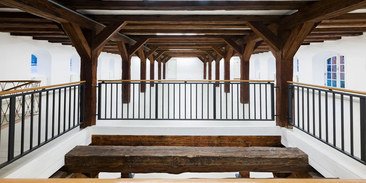 Indvendigt af et bygningsværk med bjælkeloft og bjælkegulv, to bænke og et højt loft med bjælker og bjælkegange