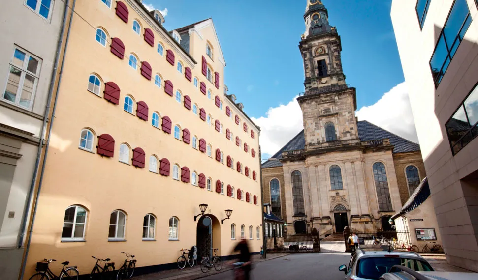 Pakhuset Strandgade i København med røde vinduesruder, hvide vindueskarm og brædder. I baggrunden ses en stor klokketårn og