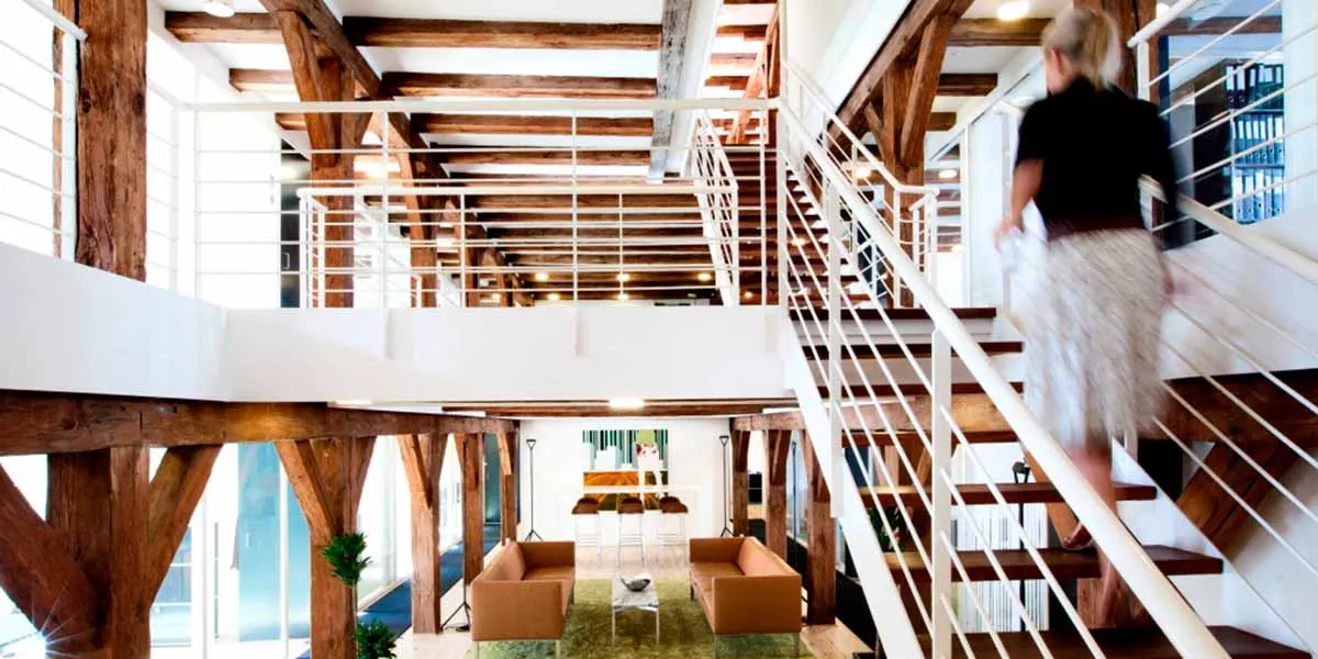 En dame går op ad en trappe i et loftsrum med træbjælker og en loftsbalkong