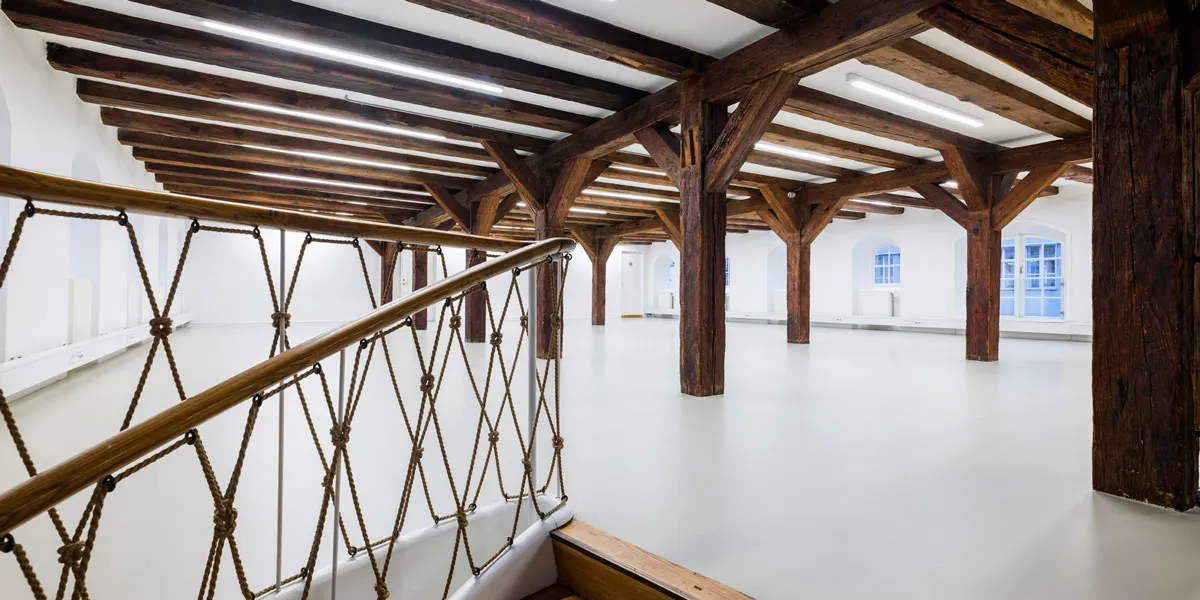 Interiør med højloftede rum, lyse bælgter og træbjælker, hvide vægge og gulve samt en bred trappe op